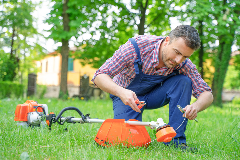 One gardener mowing grass fixing brush cutter problem