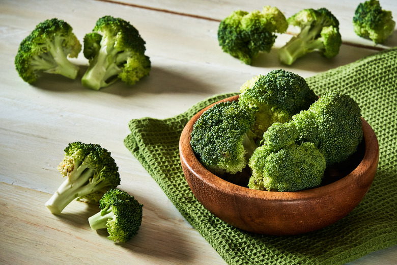 Fresh raw broccoli in bowl on rustic table.