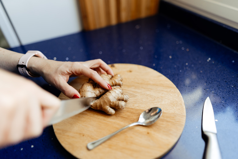 Someone cutting fresh ginger root on a cutting board.