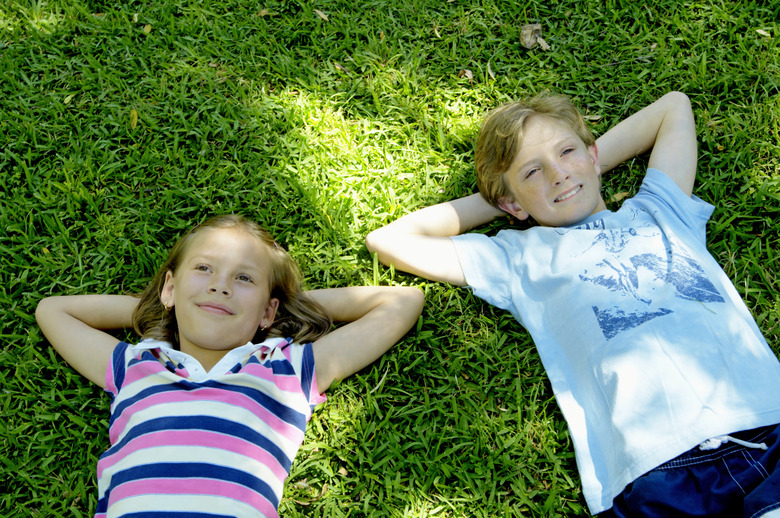 Girl and boy (9-11) lying on grass, hands behind heads, smiling