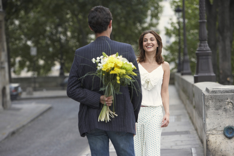 France, Paris, young couple outdoors, man holding flowers behind back