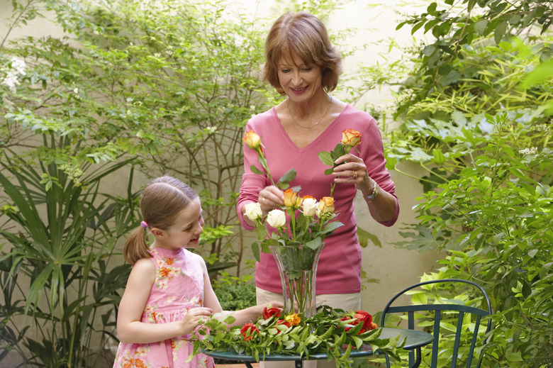 Grandmother and granddaughter (6-8) arranging flowers in vase, smiling